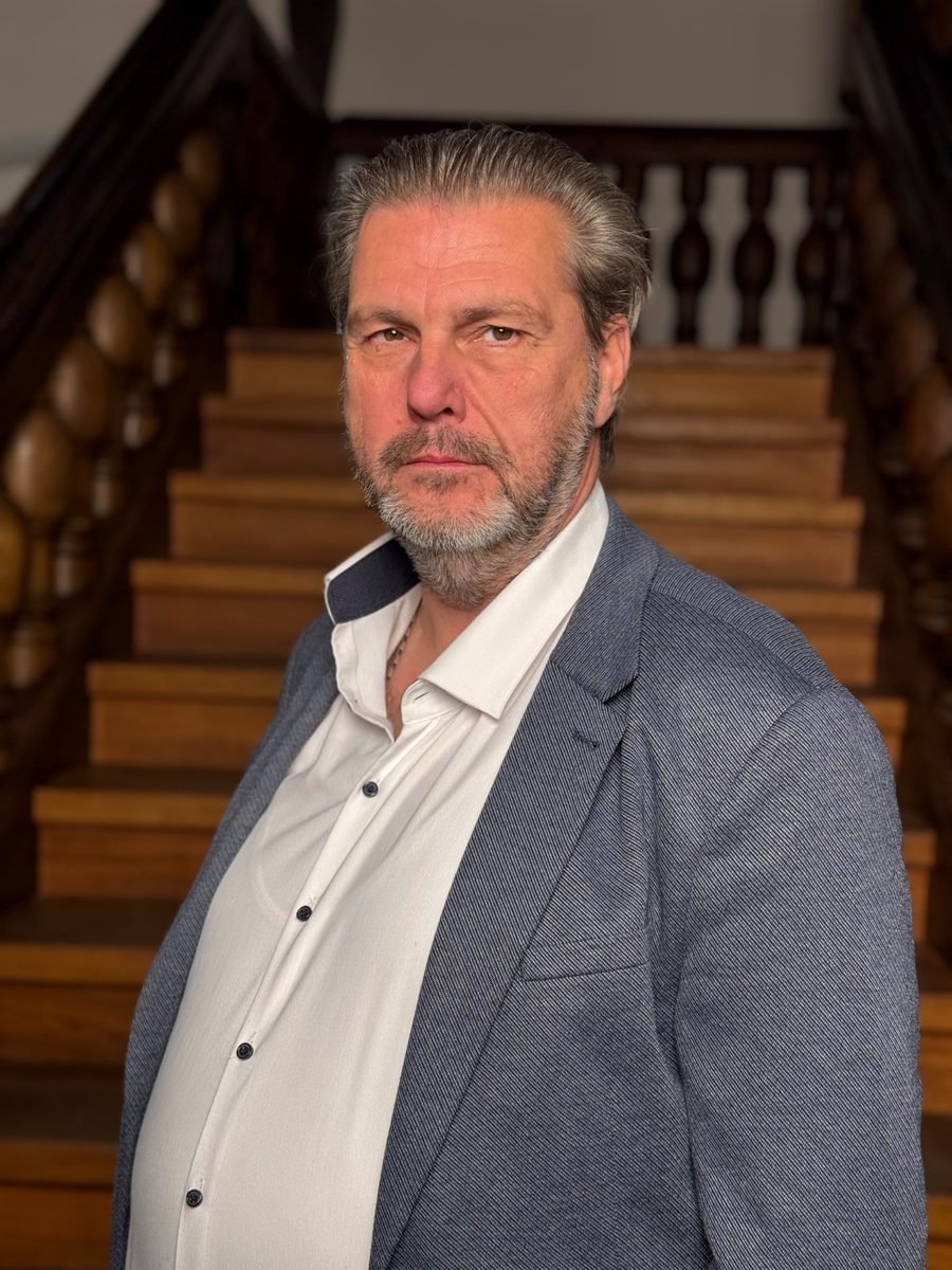 Ralf Skrzipietz im grauen Sakko vor einer Holztreppe