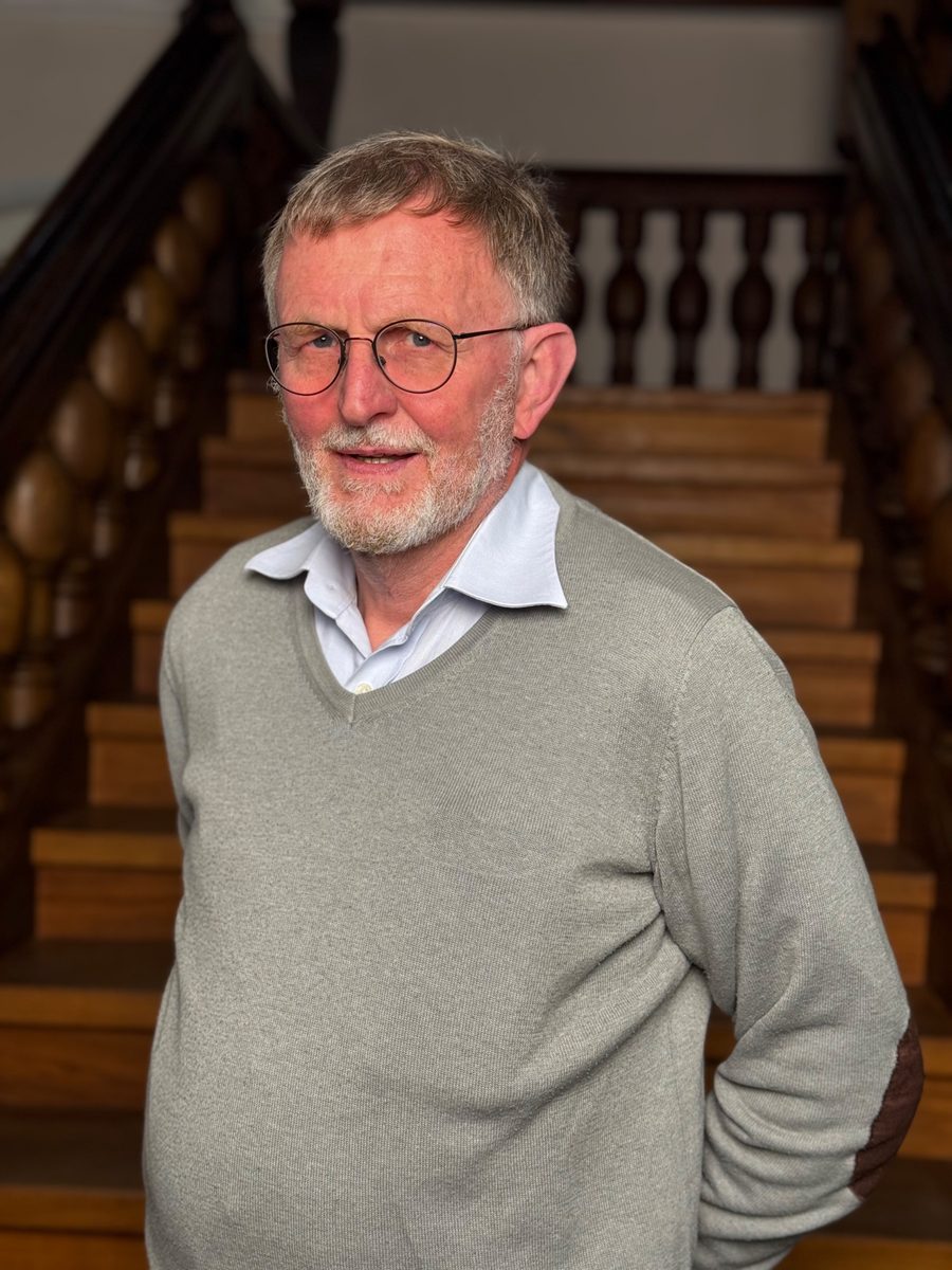Werner Fischer mit Brille und grauem Pullover vor einer Holztreppe